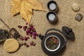 Autumn print with asian style black metal teapot with rose tea and green tea, fallen leaves, stones and small cups in the basket Royalty Free Stock Photo