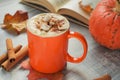 Autumn pumpkin spice latte with cream in bright orange mug on grey table. An open book and cinnamon sticks in soft focus in Royalty Free Stock Photo