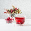 Autumn red herbal tea in transparent cup, spoon with hawthorn, rosehip berry, dried leaves in sun beam in soft light white. Royalty Free Stock Photo