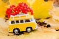 Autumn retro yellow van bus with with rowan berries on autumn maple leaf background. Funny retro toy car