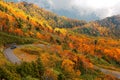 Autumn scenery of cars driving on a sharp turn of a highway winding thru colorful forests by the mountainside