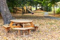 Autumn in park with wooden table and benches, path and playground. Trees with fallen colored leaves on the ground during fall Royalty Free Stock Photo