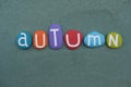 Autumn season word composed with hand painted stone letters over green sand