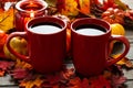 Autumn setting with small pumpkins and a red candle holder emitting light on two cups of morning coffee