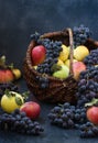 Autumn still life with apples and grapes located on a dark background, Apples and grapes in a basket Royalty Free Stock Photo