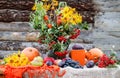 Autumn still life: a bouquet of bright yellow flowers with branches of ripe mountain ash on the table, next to vegetables and Royalty Free Stock Photo