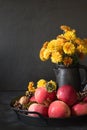 Autumn still life. Fall harvest with apples, yellow flowers in vase on dark. Royalty Free Stock Photo