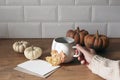 Autumn still life. Female hand in sweater holding cup of coffee in sunlight kitchen. Greeting card mockup with pumpkins