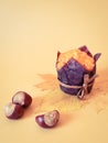 Autumn still life with pastries. Muffin in brown baking paper with chestnuts on autumn leaves on a plain beige background