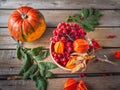 Autumn still life with pumpkin, rowan and physalis in a ceramic arrow in orange tones on an unpainted wooden table