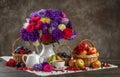 Autumn still life. A vase with asters, baskets of fruit, apples and plums and porcelain teaware on the table Royalty Free Stock Photo