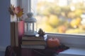 Autumn still life on a window sill. Pile of books, plaid, pumpkin, lamp, leaves and cones