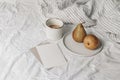 Autumn, summer breakfast in bed composition. Cup of coffee, blank greeting card mockup and pear fruit on ceramic plate