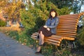 Autumn sunny day in the evening in the park, a young lady sits on a park bench, colorful autumn leaves create an incredibly cozy