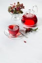 Autumn teatime with red herbal tea in transparent tea pot, cup with hawthorn berries, rose hip, dry leaves in sunlight on white. Royalty Free Stock Photo