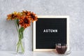 Autumn text on black letter board, bouquet of orange flowers in vase and cup of tea on table against grey stone wall. Template for Royalty Free Stock Photo