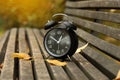 Autumn time. Alarm clock on bench in park, closeup Royalty Free Stock Photo