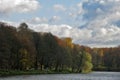 Autumn trees along the pond and cloudy day sky. Bridge away at the lake in the woods. Autumn landscape with colorful trees near Royalty Free Stock Photo