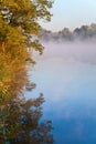 Autumn forest with bright foliage reflected in blue water of the river Dnipro, fog over the river, sunny morning. Ukraine Royalty Free Stock Photo