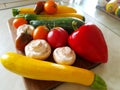 Vegetables on a cutting board on the kitchen table. Zucchini, tomatoes, champignons, peppers. Red, yellow, orange. Vegetable still