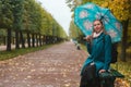 Autumn and walk. A blond woman sitting with umbrella in the Park on a bench. Alley with trimmed trees and rain