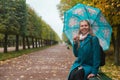 Autumn and walk. A blond woman sitting with umbrella in the Park on a bench. Alley with trimmed trees and rain. Close up