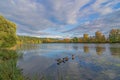 Sunny autumn day. White clouds in the blue sky over the river and trees in the park Royalty Free Stock Photo