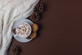 Autumn and winter concept. Top view of cup of cocoa with marshmallows, cookies, white sweater and pine cones on brown background.