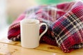 Autumn winter cozy composition. Plaid steaming white color cup of hot tea on wood table.concept of coziness and interior. Front