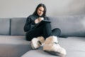 Autumn winter portrait of young girl in warm knitted sweater at home on the sofa with a digital tablet and cup of hot drink Royalty Free Stock Photo