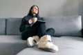 Autumn winter portrait of young girl in warm knitted sweater at home on the sofa with a digital tablet and cup of hot drink Royalty Free Stock Photo