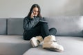 Autumn winter portrait of young girl in warm knitted sweater, at home on sofa with digital tablet and phone Royalty Free Stock Photo