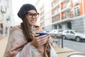 Autumn winter portrait of young smiling woman in hat, with cup of hot drink. City street background Royalty Free Stock Photo