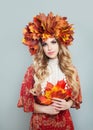 Autumn woman in fall leaves crown holding red leaves in hands on gray background. Pretty model with blonde curly hair and makeup