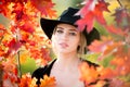 Autumn woman with yellow maple leaves. Closeup portrait of a beautiful girl in black hat near colorful autumn leaves Royalty Free Stock Photo