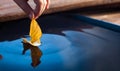 Autumn yellow leaf ship in children hand in water. Boy in park play with boat in river