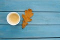 an autumn yellow oak leaf in a paper cup stands on the table on a blue background Royalty Free Stock Photo