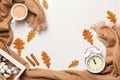 Autumnal cosiness concept. Beige cashmere scarf coffee cup alarm clock with autumn oak leaves on a light gray background.