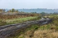 autumnal foggy morning rustic lansdcape with dirt road in the foreground and small buildings on hill in the background