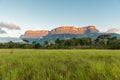 Auyantepuy bathed in orange sunlight from sunset over green Savannah