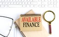 AVAILABLE FINANCE text in office notebook with keyboard, magnifier and glasses , business concept