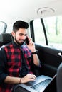 Always available. Handsome young indian man working on his laptop and talking on the phone while sitting in the car Royalty Free Stock Photo