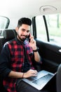 Always available. Handsome young indian man working on his laptop and talking on the phone while sitting in the car Royalty Free Stock Photo