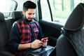 Always available. Handsome young indian man working on his laptop and typing on the phone while sitting in the car Royalty Free Stock Photo