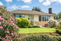 Average family house with rhododendron flowers in front on cloudy sky background