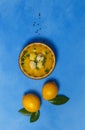 Greek avgolemono soup in a bowl and two lemons with leaves, on a bright blue background. Top view, copy of the space, vertically