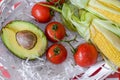 Avocado, branch of tomatoes and two cobs of sweet corn in white wooden basket with straw