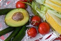 Avocado, cucumbers, branch of tomatoes and two cobs of sweet corn in white wooden basket with straw