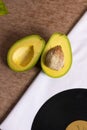 Avocado cut in half ready to eat on table with black long play disk in a corner