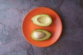 Avocado halves lie on an orange plate on a slate Royalty Free Stock Photo